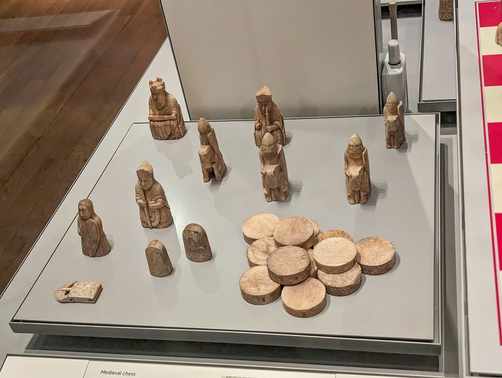 Carved historic chess pieces displayed in a museum case on a wooden surface