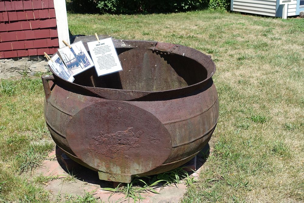 An antique maritime compass resting on a worn wooden deck beside coiled hemp nautical rope.